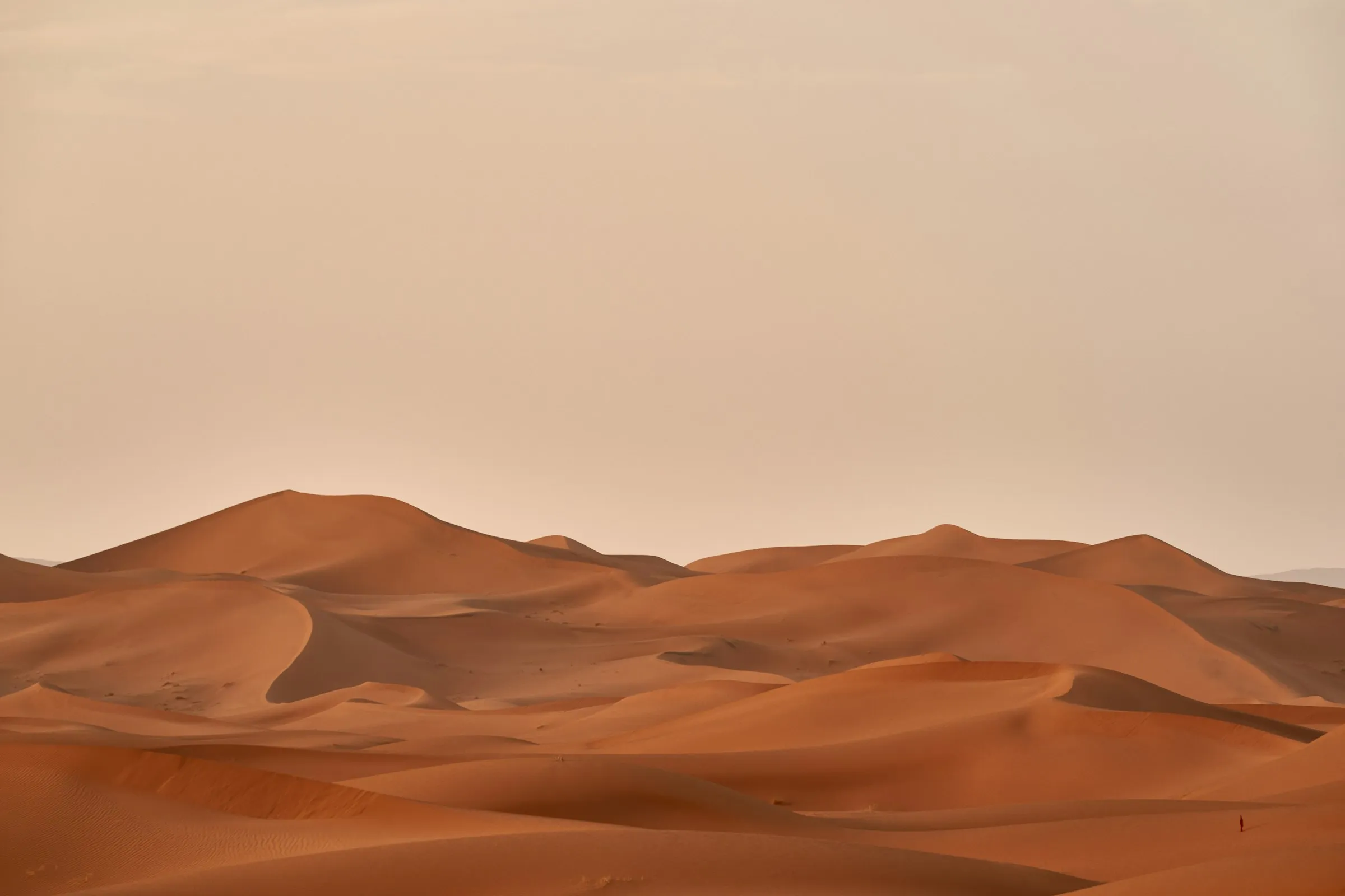 Orange sand dunes under a pale evening sky, with one person walking far away